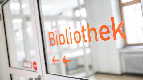 Photo of orange foil lettering "Library" and arrows on a glass door.