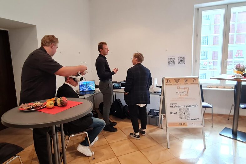 An einem Tisch stehend präsentieren Ansgar Rahmacher, Marcel Mitas und Leon Sachweh Assistenzsystem für die Gesundheits- und Pflegebranche.