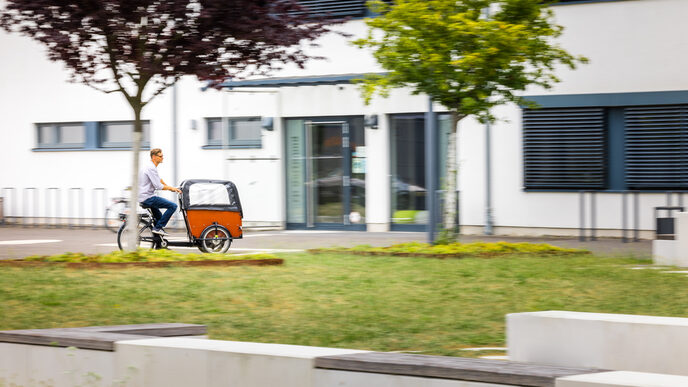 Foto Foto von einem Mann auf einem Lastenfahrrad auf dem FH-Gelände fährt.