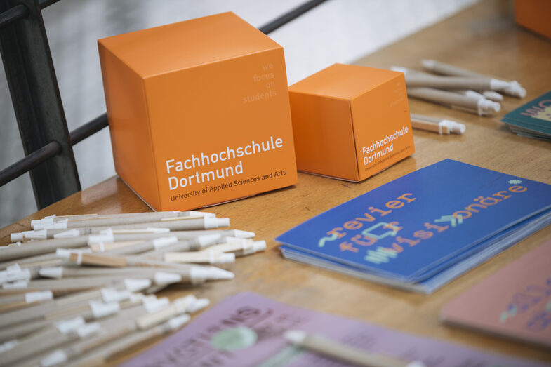 There are two FH cubes in orange on a table, surrounded by pens, flyers and brochures