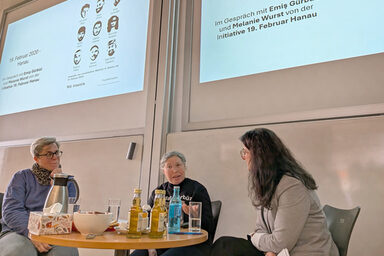 Menschen vor einer Leinwand in einem Hörsaal sprechen miteinander.