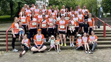 Auf einer Treppe stehen und sitzen mehrere Erwachsene und Kinder. Die meisten tragen ein Shirt mit orangefarbenen und weißen Elementen.