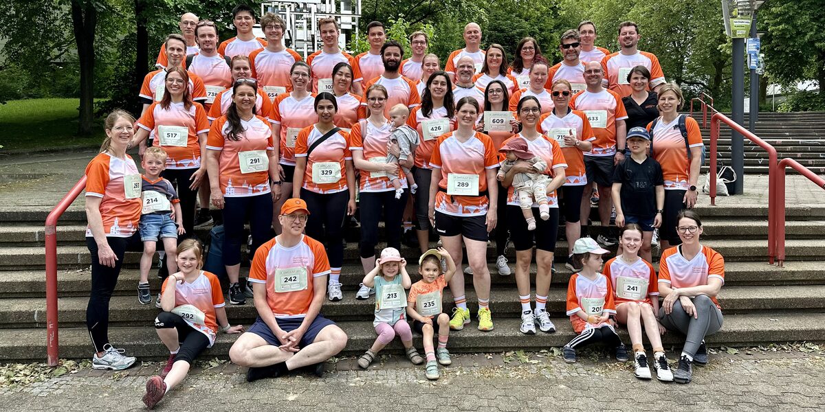 Auf einer Treppe stehen und sitzen mehrere Erwachsene und Kinder. Die meisten tragen ein Shirt mit orangefarbenen und weißen Elementen.