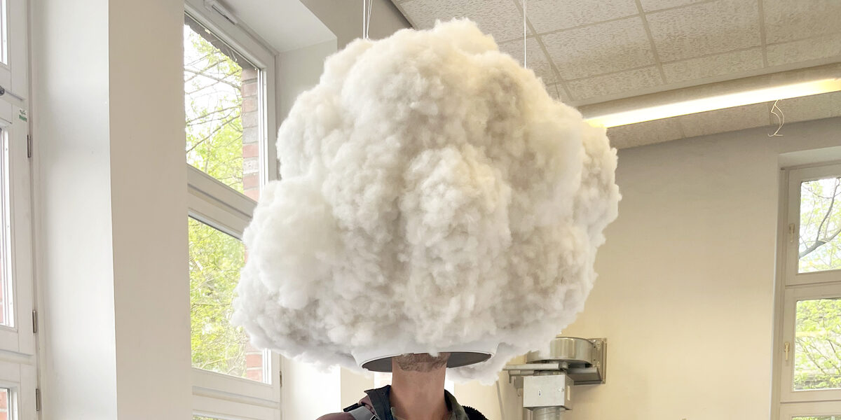 A person stands under a cloud-like structure that has an opening at the bottom so that it encloses the person's head.