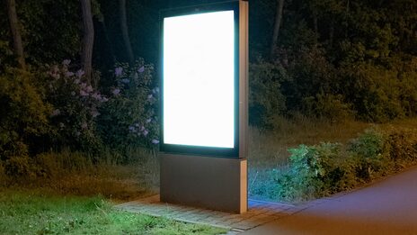 An advertising display lights up in front of a dark wooded area.