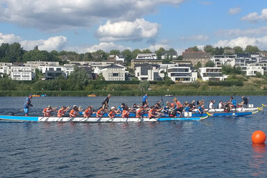 Auf einem See fahren mehrere Boote mit jeweils vielen Paddlern.