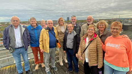 A group stands on a platform high above the rooftops of the city. The skyscrapers of Dortmund can be seen in the background.