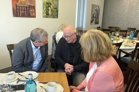 Personen sitzen um einen Kaffee-Tisch und unterhalten sich.