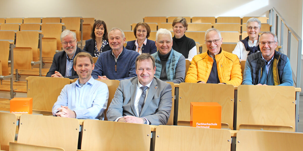 Mehrere Personen sitzen in einem Hörsaal auf drei Reihen verteilt.