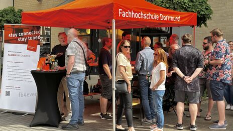 Absolvent*innen stehen am Alumni-Stand des Fachbereichs und unterhalten sich.