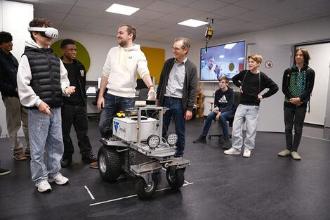 Menschen stehen um einen Roboter, einer trägt eine VR-Brille.