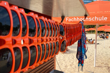 Sunglasses from Fachhochschule Dortmund hang in a row. A beach with parasols and leagues can be seen in the background.