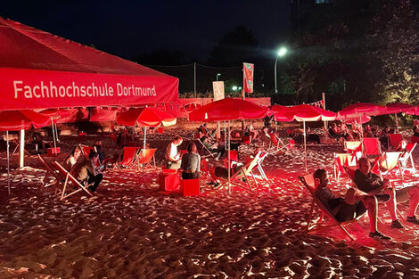 People sit under the FH parasols on the sun loungers on the beach at night at the Juicy Beats Festival.