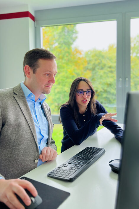 Two people are together in front of a monitor and analyze the data on the screen.