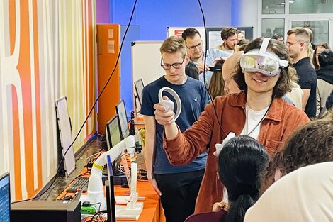 Eine Gruppe Menschen schaut sich verschiedene Geräte an. Eine Person hat eine VR-Brille auf.