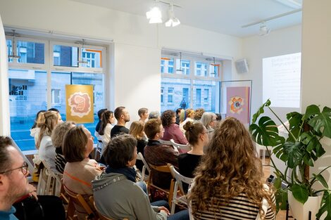 Die Besucher*innen sitzen während eines Vortrags in der Nordstadtgalerie vor einer Bühne.