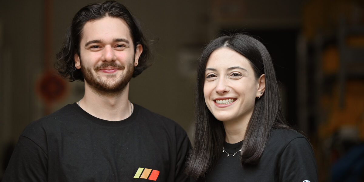 Zwei Personen in schwarzen T-Shirts im Porträt vor einem dunklen Raum im Hintergrund.