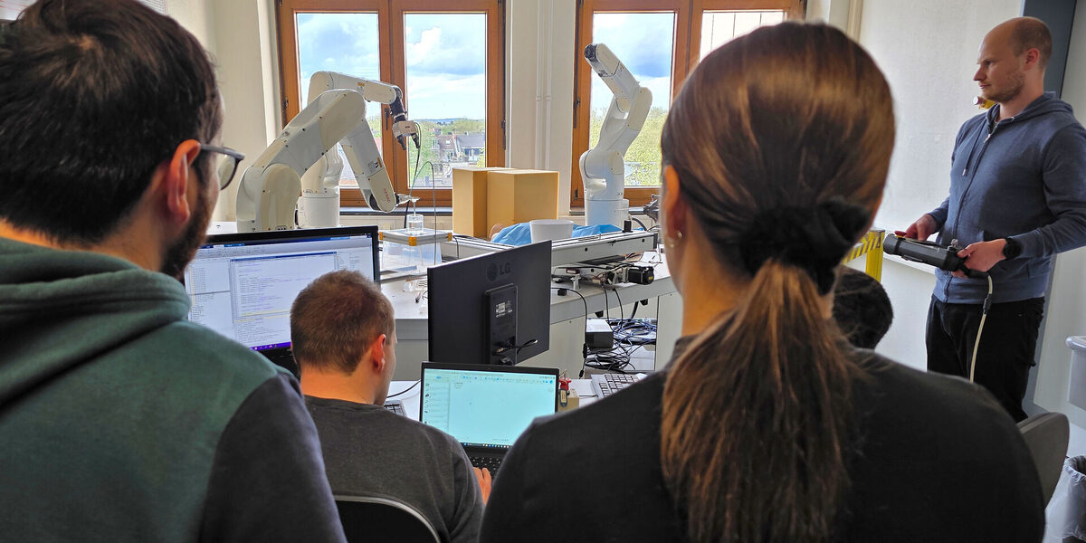 Zwei Personen schauen weiteren Personen zu, die Roboter-Arme steuern.