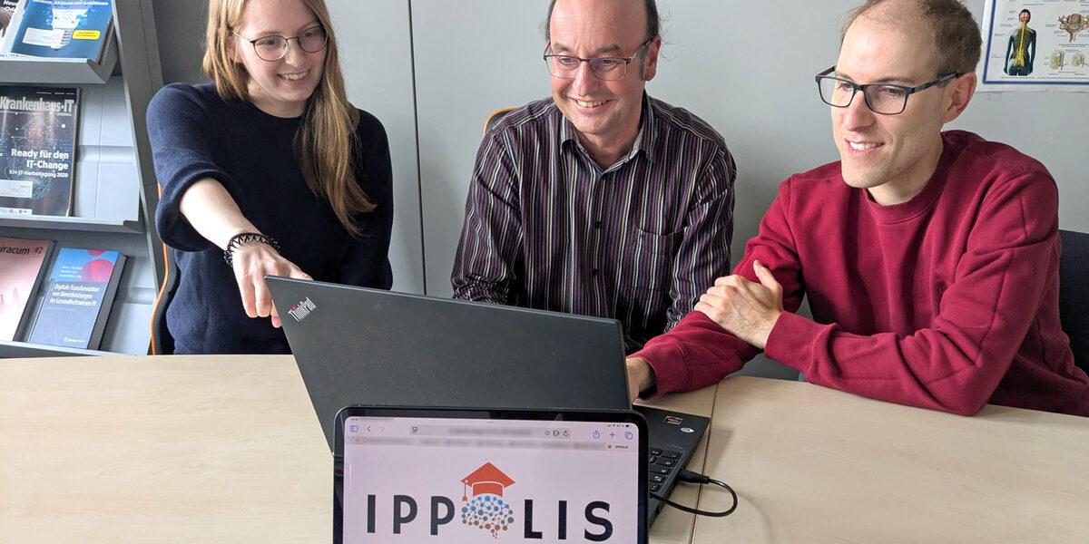 Drei Personen sitzen vor einem Laptop. Auf einem Monitor davor ist das Logo „IPPOLIS“ zu sehen.