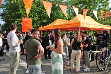 People stand at the summer party of the Faculty of Architecture at Fachhochschule Dortmund. Under orange pavilions, the student council provides guests with drinks.