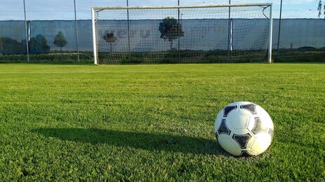 A soccer ball lies on the grass of a soccer field in front of a goal.