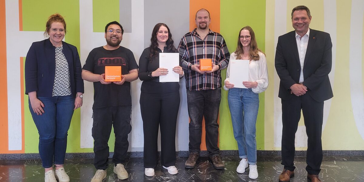 Six people stand in a row in front of a wall with brightly colored areas. Two people are holding a FH cube in front of them, two people are holding a white folder.