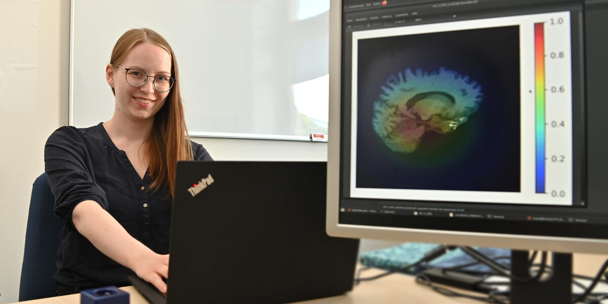 A person is sitting at a notebook, a brain scan can be seen on the monitor next to them.