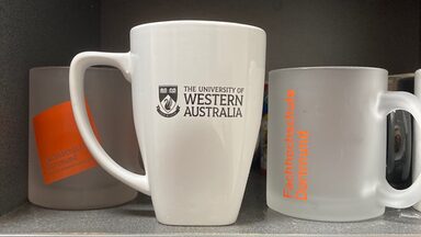 Two mugs with Fachhochschule Dortmund on a shelf with a mug bearing the UWA logo