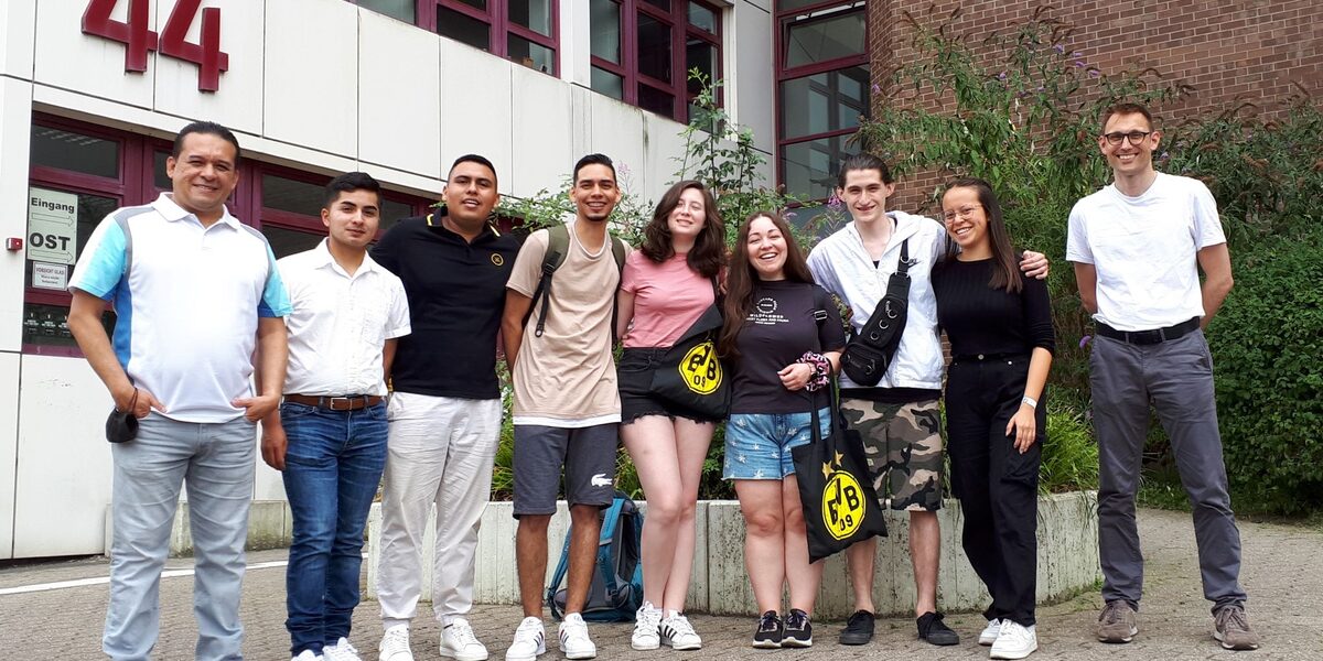 Nine people stand in front of the entrance to a university building.