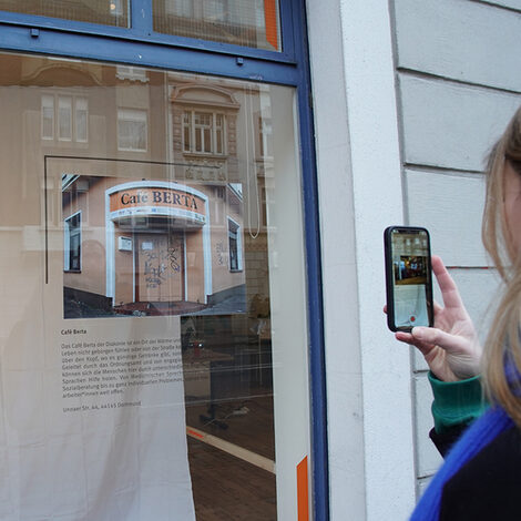 Eine Person scannt mit der Foto-App auf ihrem Smartphone die Ausstellungsinhalte im Schaufenster