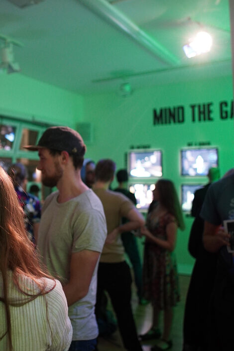 Numerous visitors stand in the green-lit gallery.