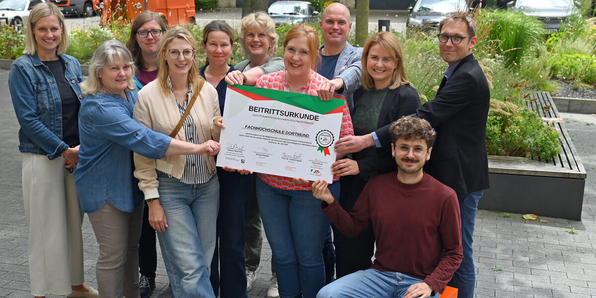 Personen stehen in einer Gruppe zusammen und halten eine große Urkunde von "Sicher im Dienst"