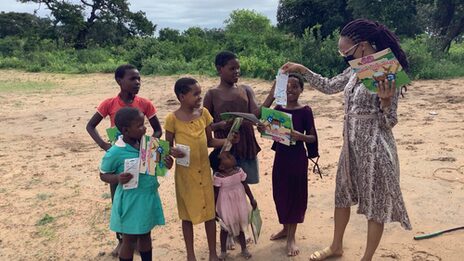 A social worker distributes the coloring book to a small group of children of different ages.