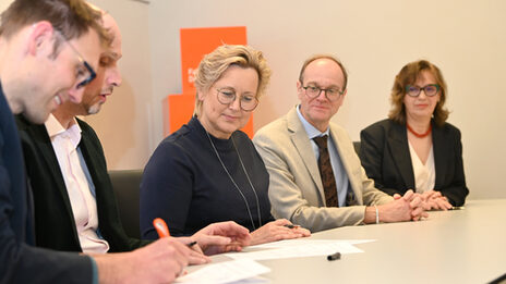 Mehreren Personen sitzen an einem Tisch, sie unterschreiben Papiere.