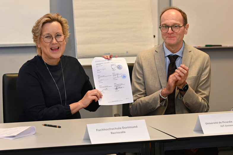 Zwei Personen halten einen unterschriebenen Vertrag hoch.