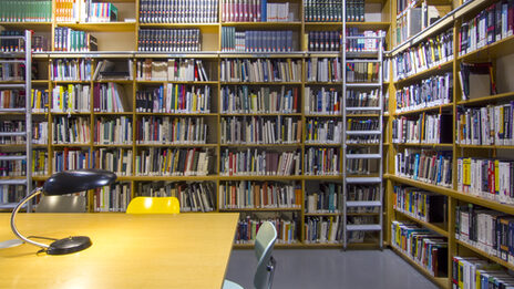 Foto des Lesesaals in der Bibliothek mit Bücherregalen, Tischen, Leselampen und Stühlen__Photo of the library reading room with book shelves, desks, reading lamps and chairs