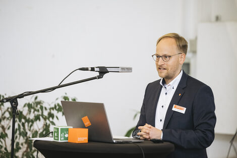 Auf dem Bild steht Prof. Dr. Franz Vogler an einem Pult mit Mikrofon an einem Ständer. Auf dem Pult steht ein Laptop und Herr Vogler redet. Der Hintergrund ist weiß