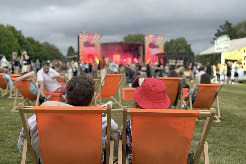 Menschen sitzen in orangenen FH-Liegestühlen und blicken auf die Bühne.