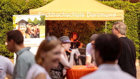 Impressions of the 2024 summer festival. Geiger stands under a tent with the words Fachhochschule Dortmund on it.