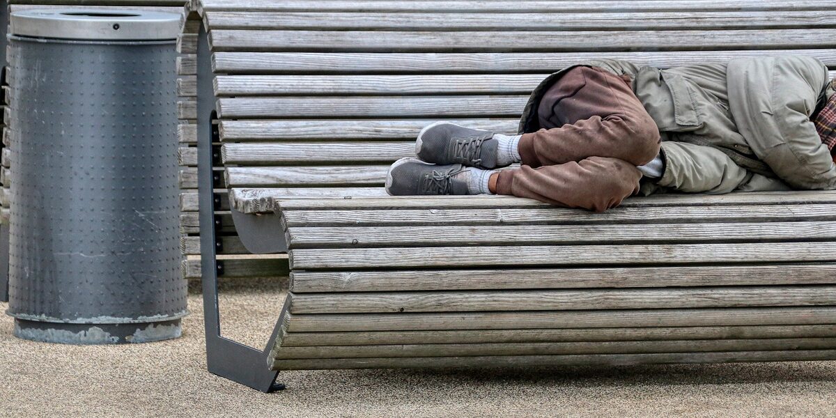 A homeless person lies on a bench