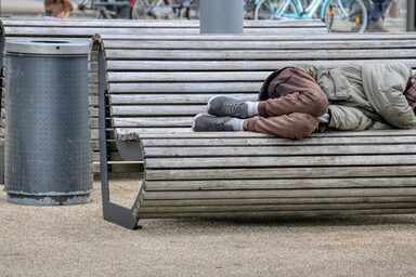 Eine wohnungslose Person liegt auf einer Bank