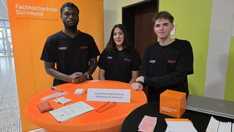 Three people are standing behind a table with various utensils.