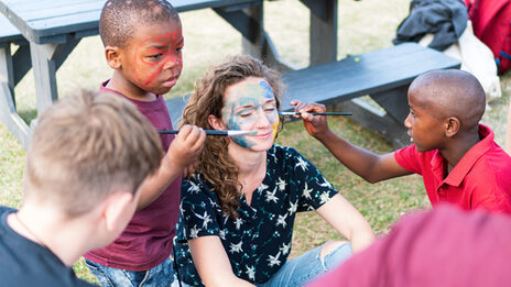 A student's face is painted with brushes by children in South Africa.