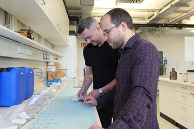 Zwei Personen stehen in einem Labor und untersuchen Proben.