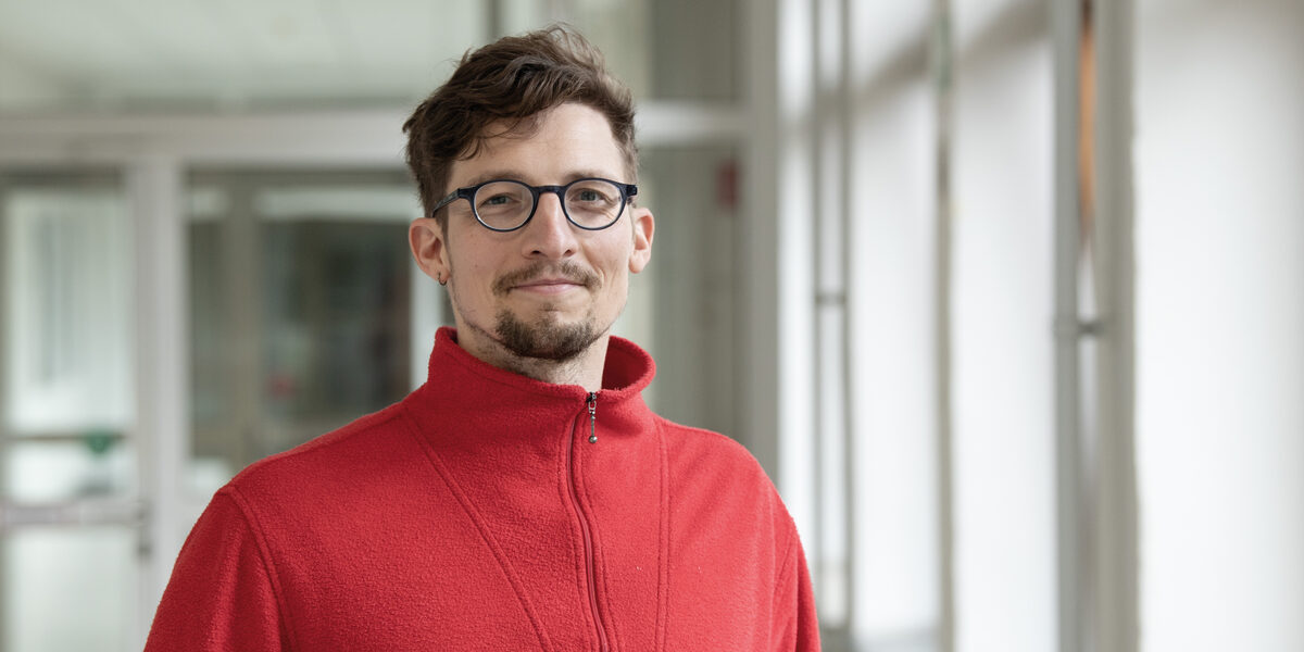 A person in a red sweater looks friendly into the camera.