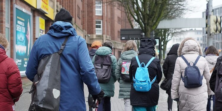 Several people with thick jackets and backpacks walk through the city.