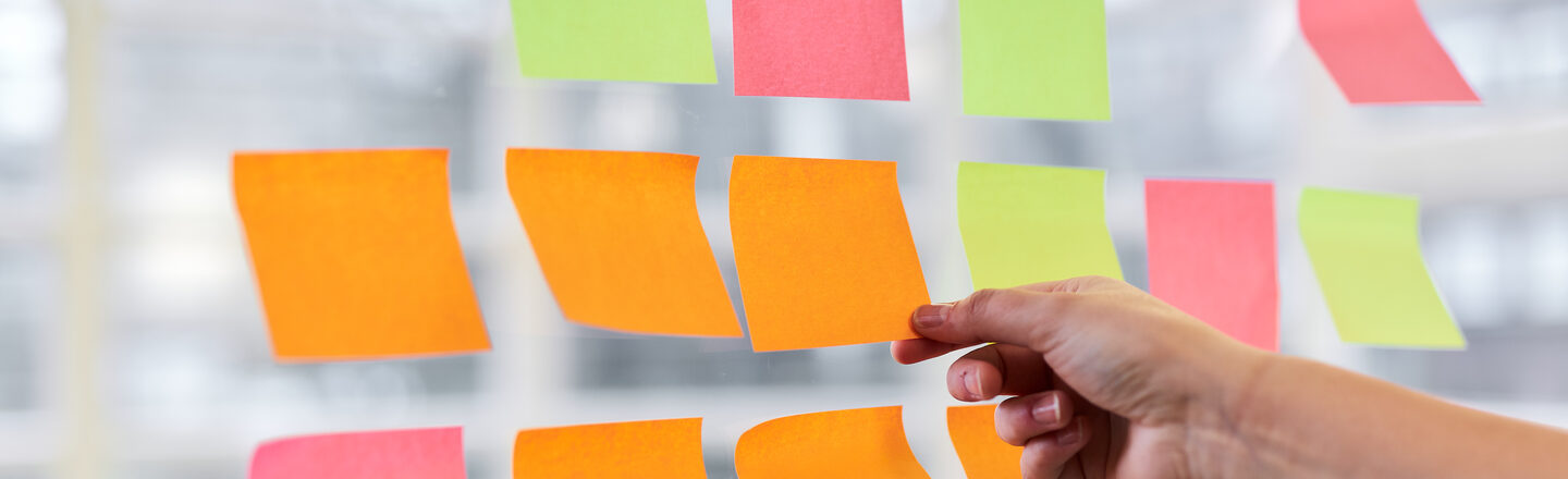 Mehrere leere Post-It kleben an einer Scheibe, eine Hand fasst einen Post-It an