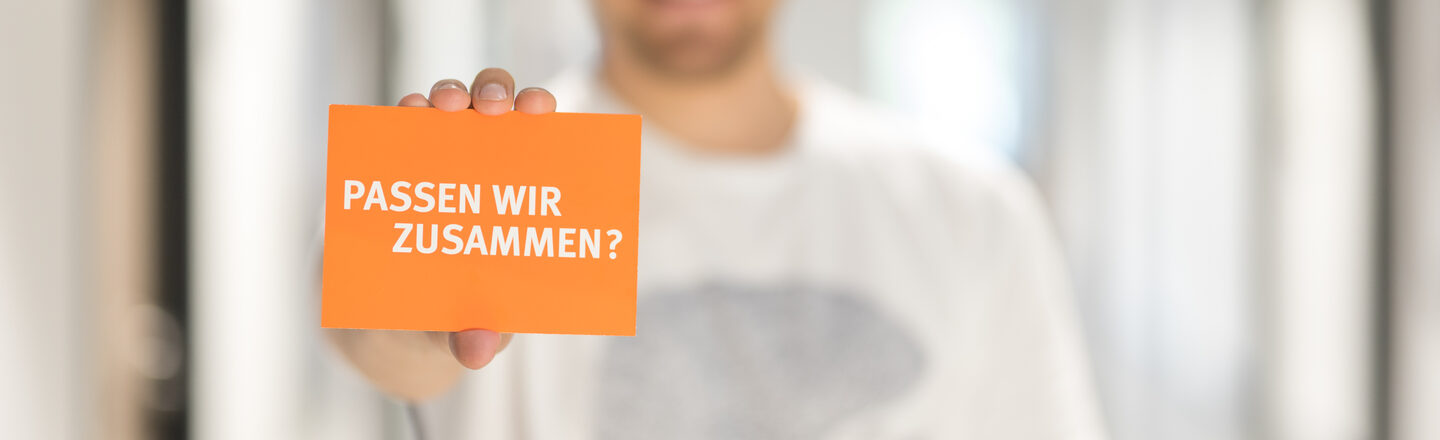 Photo of a man holding a card with the words "Do we fit together?" into the camera __Man out of focus holding a card with the words "Do we fit together?" into the camera.