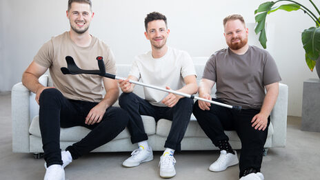 Three people are sitting on a sofa and holding a crutch.