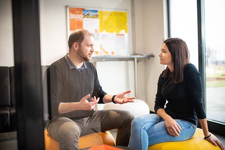Photo of a TalentScout and a pupil sitting on beanbags and chatting. In front of them on a side table are some orange folders.